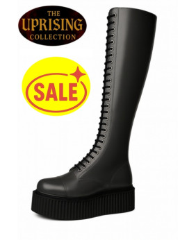 Stivale alto donna in pelle nera con zeppa spessa, fodera liscia e lacci frontali; etichette promozionali “THE UPRISING COLLECTION” e simbolo di vendita.